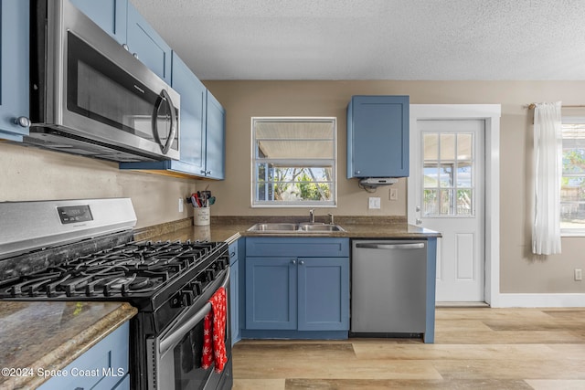 kitchen with appliances with stainless steel finishes, light wood-type flooring, a textured ceiling, blue cabinets, and sink