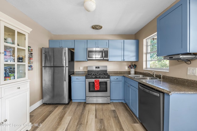 kitchen featuring blue cabinets, sink, light hardwood / wood-style flooring, a textured ceiling, and stainless steel appliances