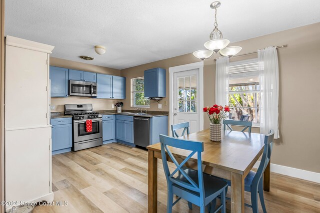 kitchen with blue cabinets, sink, light wood-type flooring, appliances with stainless steel finishes, and decorative light fixtures