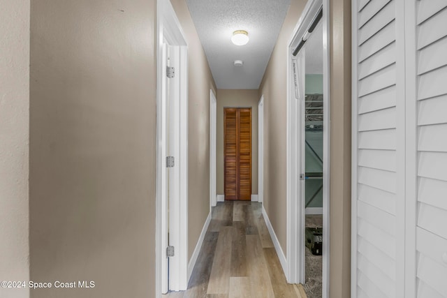 hall with a textured ceiling and light hardwood / wood-style flooring