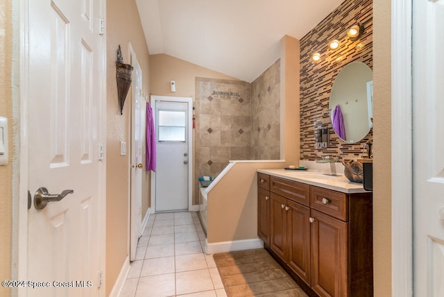 bathroom with tile patterned flooring, a tile shower, vanity, and vaulted ceiling