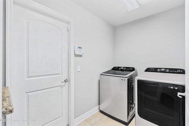 washroom with washing machine and dryer, light tile patterned floors, and a textured ceiling