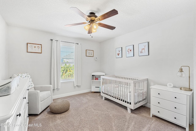 carpeted bedroom with a crib, a textured ceiling, and ceiling fan