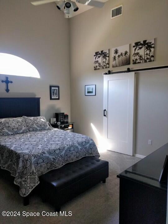 bedroom with carpet flooring, a barn door, ceiling fan, and a high ceiling