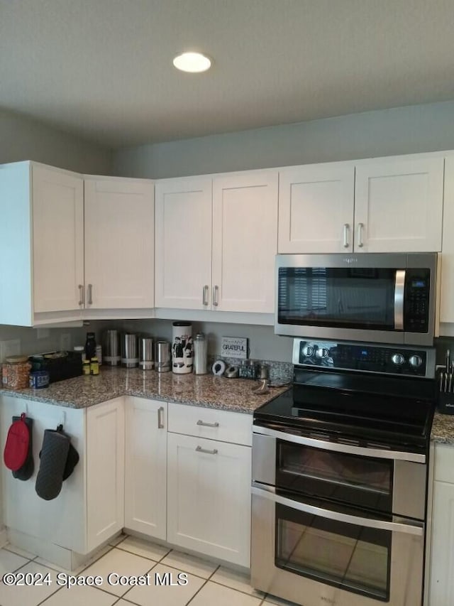 kitchen featuring appliances with stainless steel finishes, light tile patterned floors, white cabinetry, and dark stone counters