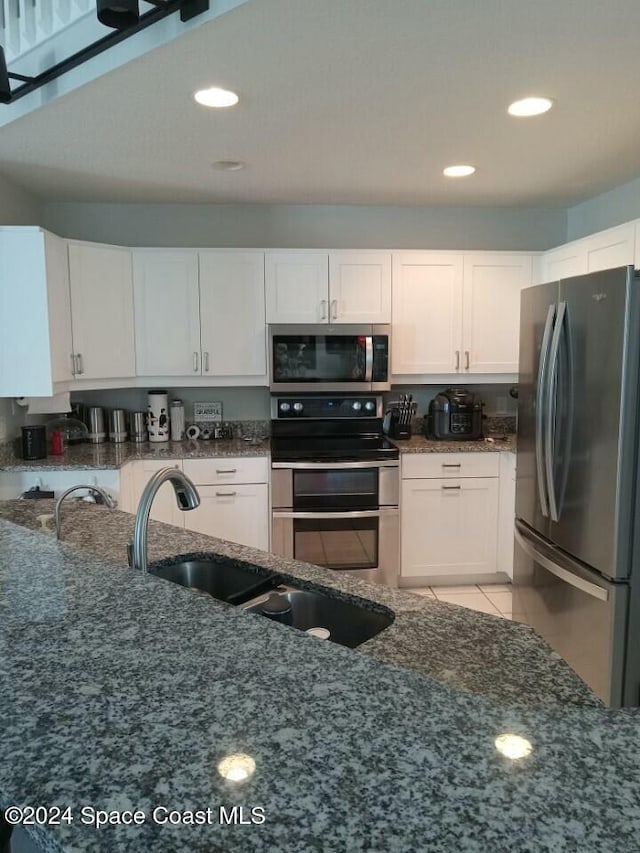 kitchen with dark stone countertops, white cabinets, light tile patterned flooring, and appliances with stainless steel finishes