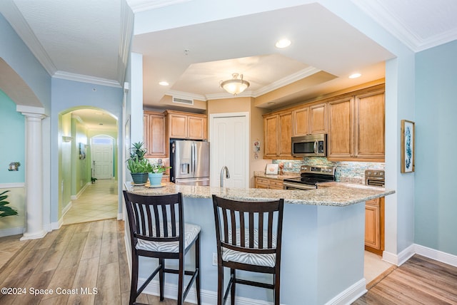 kitchen featuring a breakfast bar, a raised ceiling, light wood-type flooring, light stone counters, and stainless steel appliances