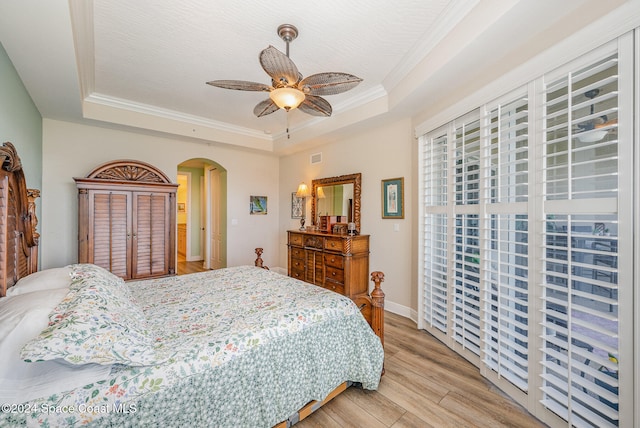 bedroom with a tray ceiling, light hardwood / wood-style flooring, ceiling fan, and crown molding