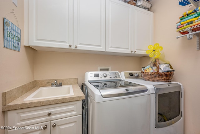 clothes washing area with separate washer and dryer, sink, and cabinets