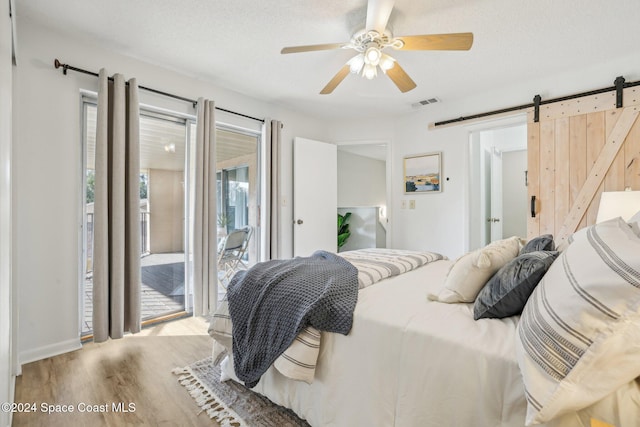 bedroom with access to exterior, a textured ceiling, ceiling fan, a barn door, and light hardwood / wood-style floors