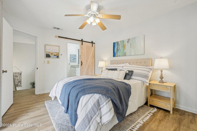 bedroom with light wood-type flooring, a barn door, ensuite bathroom, and ceiling fan