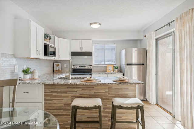 kitchen with white cabinets, a wealth of natural light, light stone countertops, and appliances with stainless steel finishes