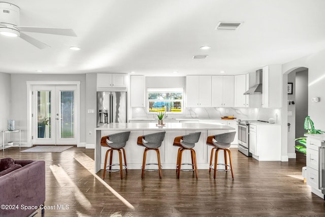 kitchen featuring white cabinets, wall chimney range hood, dark wood-type flooring, and appliances with stainless steel finishes