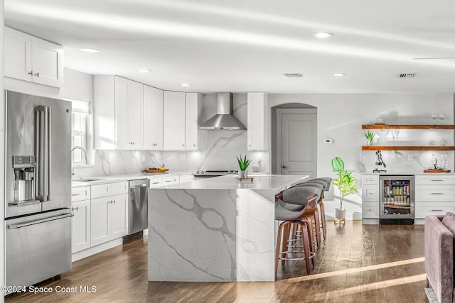 kitchen featuring appliances with stainless steel finishes, wine cooler, wall chimney exhaust hood, a center island, and white cabinetry