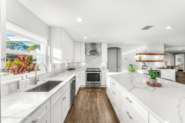 kitchen with white cabinets, light stone counters, wall chimney range hood, and stainless steel appliances