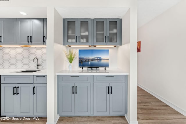 bar with decorative backsplash, light wood-type flooring, gray cabinets, and sink