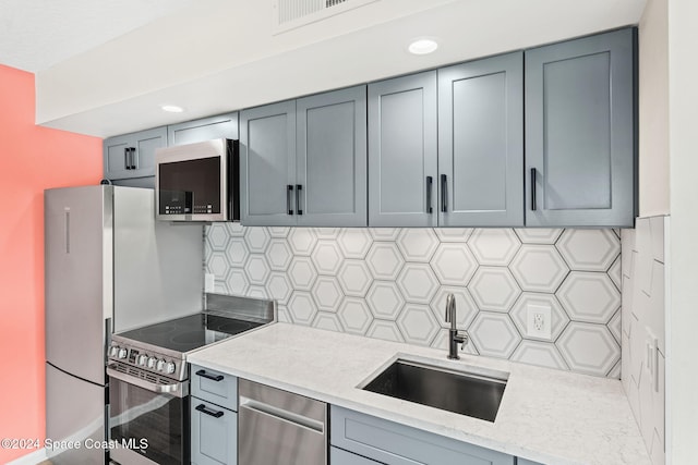 kitchen featuring gray cabinetry, sink, light stone countertops, tasteful backsplash, and stainless steel appliances