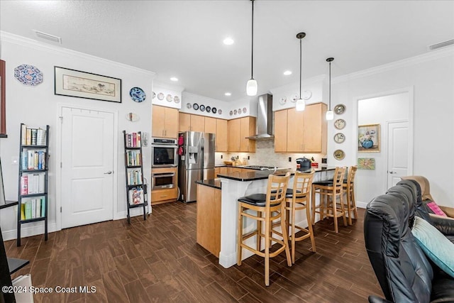 kitchen with wall chimney range hood, hanging light fixtures, a kitchen bar, kitchen peninsula, and stainless steel appliances