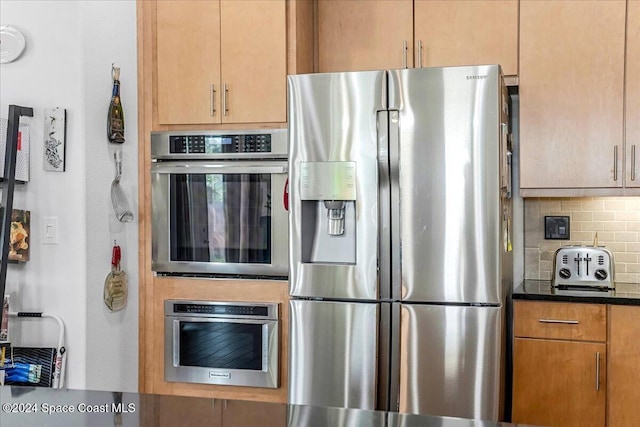 kitchen with backsplash, stainless steel appliances, and dark stone counters