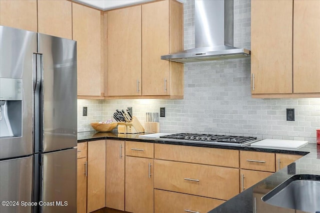 kitchen featuring decorative backsplash, light brown cabinets, wall chimney range hood, and appliances with stainless steel finishes