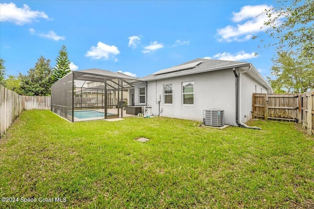 rear view of property featuring a lawn, solar panels, a lanai, central AC, and a fenced in pool