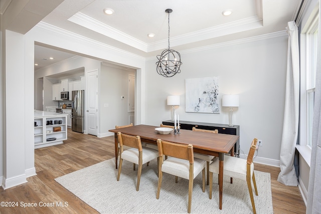 dining space with a notable chandelier, a raised ceiling, light wood-type flooring, and ornamental molding