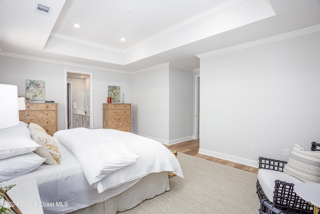 bedroom with hardwood / wood-style floors, ensuite bathroom, a tray ceiling, and crown molding