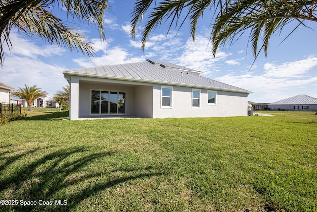 back of property with a yard, metal roof, and stucco siding