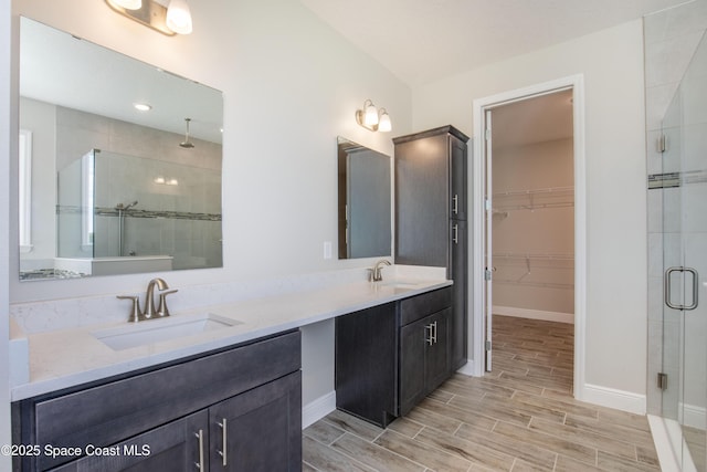 full bathroom featuring double vanity, a stall shower, wood tiled floor, and a sink