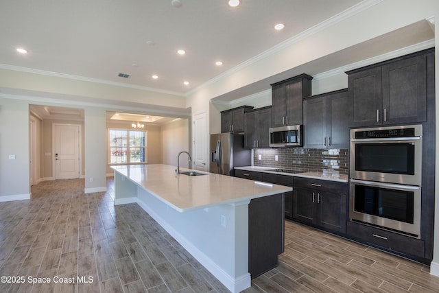 kitchen featuring wood finish floors, an island with sink, a sink, decorative backsplash, and stainless steel appliances