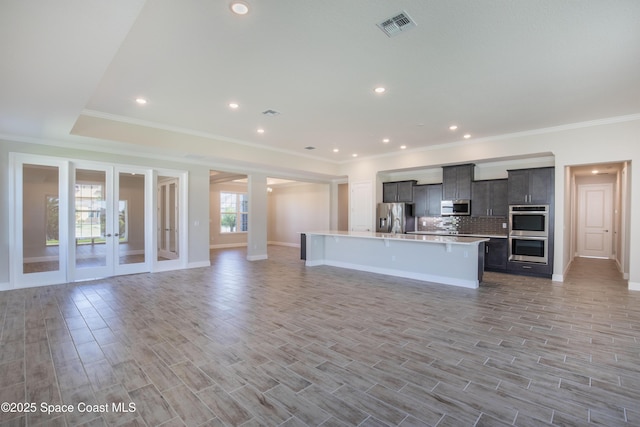 kitchen featuring visible vents, a kitchen island with sink, stainless steel appliances, light countertops, and open floor plan