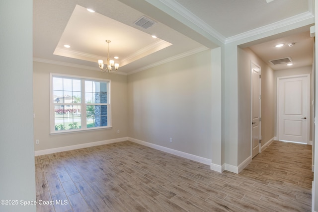 spare room featuring a tray ceiling, light wood-style floors, visible vents, and a chandelier