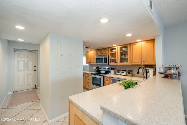 kitchen with kitchen peninsula, appliances with stainless steel finishes, tasteful backsplash, a textured ceiling, and light tile patterned floors