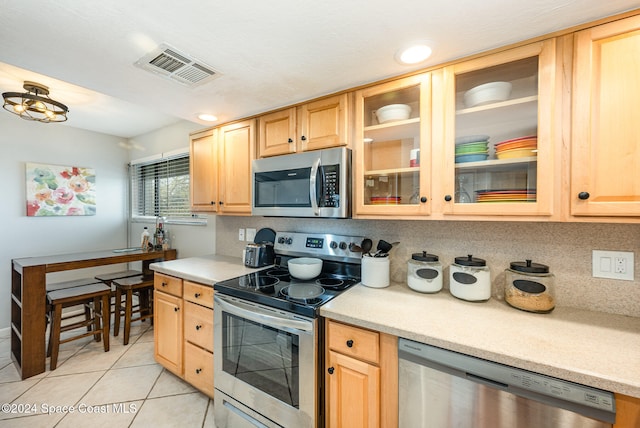 kitchen featuring tasteful backsplash, light brown cabinetry, light tile patterned floors, and appliances with stainless steel finishes