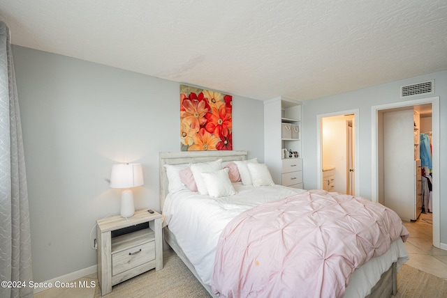 bedroom with ensuite bathroom, light tile patterned flooring, and a textured ceiling