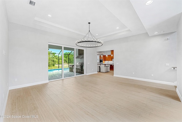 unfurnished living room featuring a notable chandelier, light wood-type flooring, and a tray ceiling