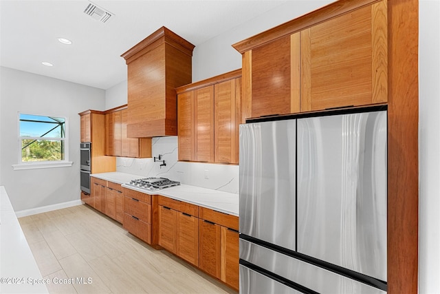 kitchen with tasteful backsplash, light stone countertops, stainless steel appliances, and light hardwood / wood-style floors