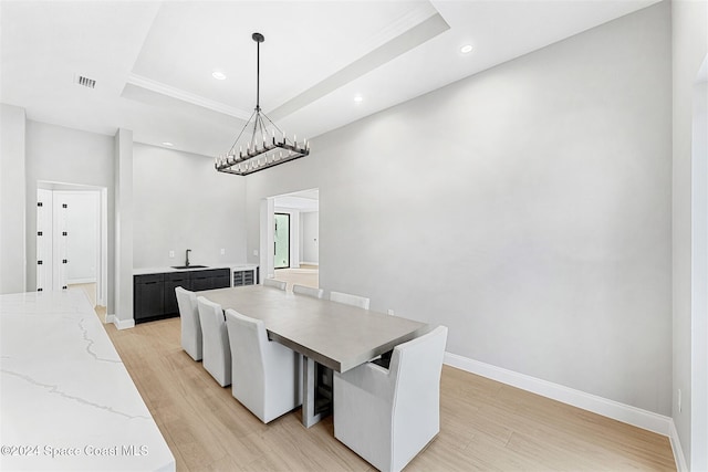 dining room with a raised ceiling, sink, a chandelier, and light wood-type flooring