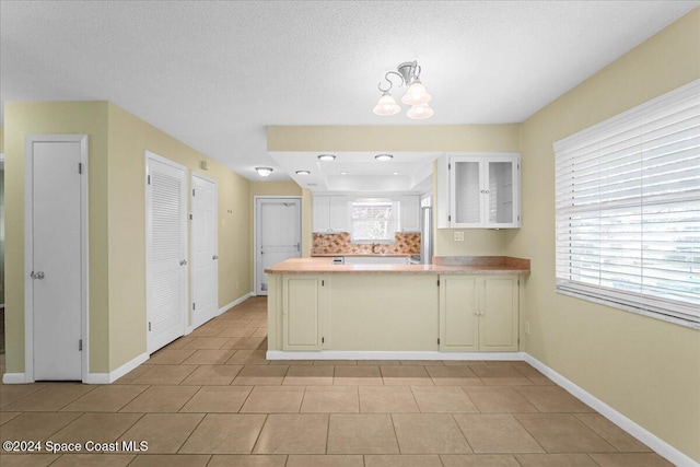 kitchen featuring kitchen peninsula, backsplash, light tile patterned floors, a notable chandelier, and white cabinets