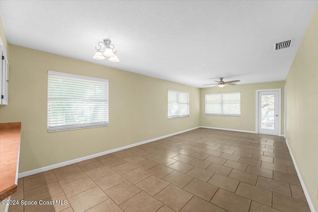 tiled empty room featuring a textured ceiling and ceiling fan with notable chandelier