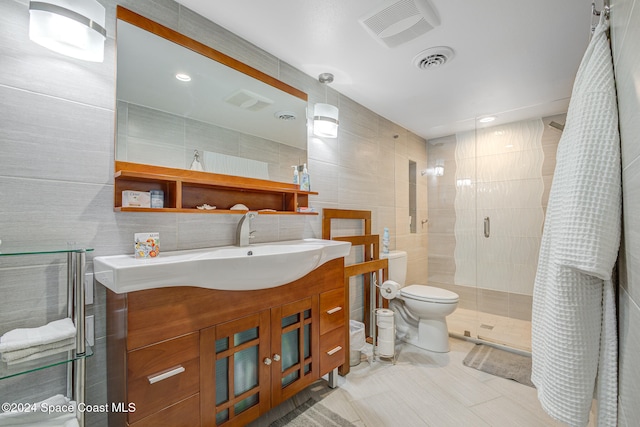 bathroom with vanity, a shower with door, toilet, and tile walls