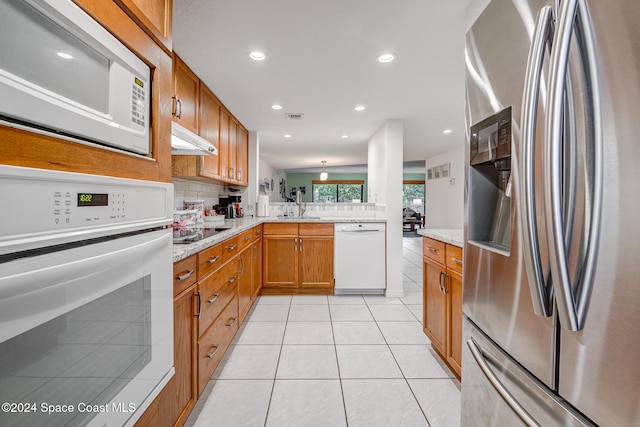 kitchen featuring kitchen peninsula, tasteful backsplash, white appliances, sink, and light tile patterned floors