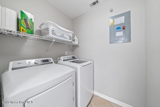 laundry area with electric panel, light tile patterned flooring, and washer and dryer