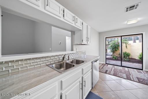 kitchen with dishwasher, sink, tasteful backsplash, light tile patterned flooring, and white cabinets