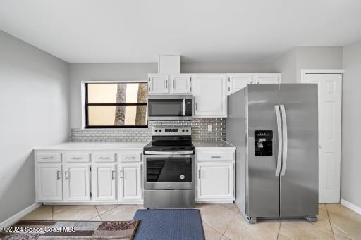 kitchen with white cabinets, appliances with stainless steel finishes, decorative backsplash, and light tile patterned floors