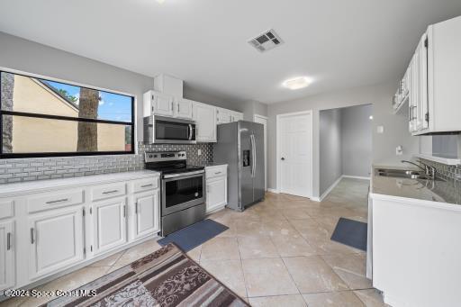 kitchen featuring decorative backsplash, stainless steel appliances, sink, white cabinetry, and light tile patterned flooring