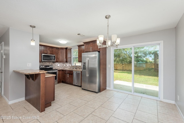 kitchen featuring kitchen peninsula, appliances with stainless steel finishes, backsplash, light stone countertops, and decorative light fixtures