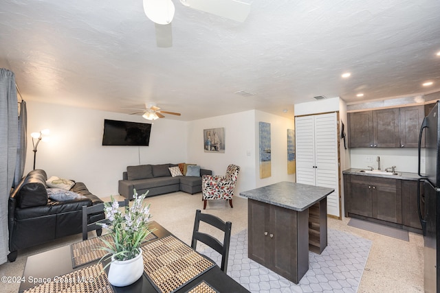 kitchen featuring dark brown cabinetry, ceiling fan, a center island, sink, and a textured ceiling