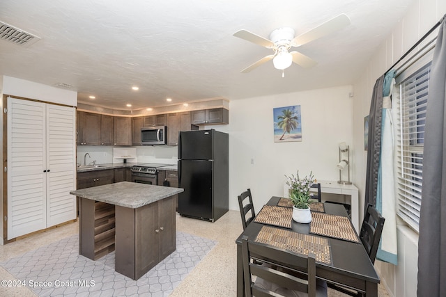 kitchen with dark brown cabinetry, ceiling fan, sink, stainless steel appliances, and a kitchen island