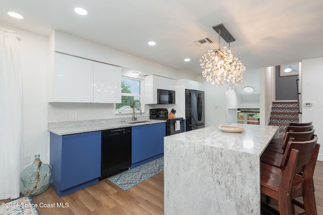 kitchen featuring pendant lighting, black appliances, light hardwood / wood-style flooring, a kitchen island, and white cabinetry